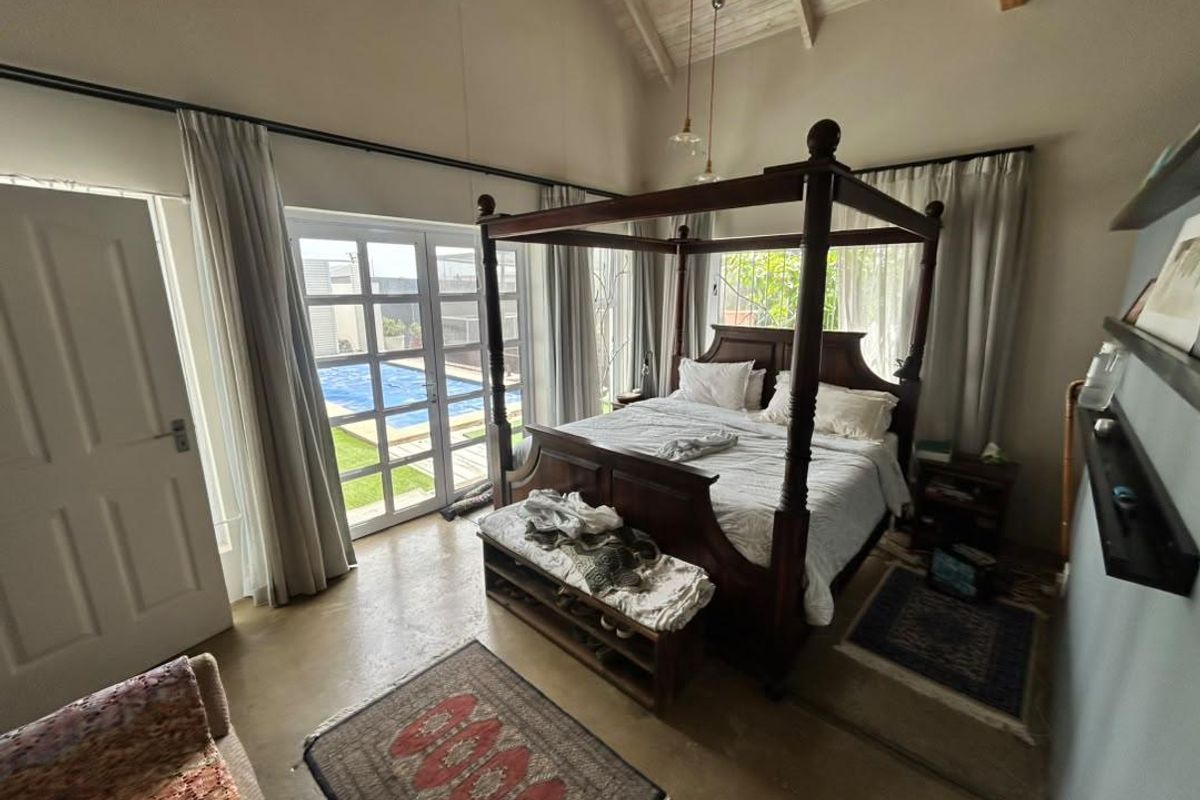 Spacious bedroom featuring a high vaulted ceiling with exposed timber beams, polished concrete floors, and direct access to the pool area via french doors.