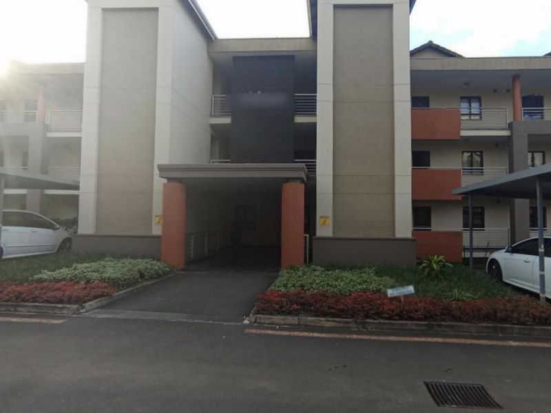 Front view of a modern apartment complex featuring covered parking bays, multi-level balconies, and well-maintained landscaped garden beds.