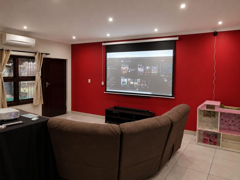 A dedicated cinema room featuring a large projector screen, tiled flooring, recessed lighting, and a wall-mounted split-system air conditioner.