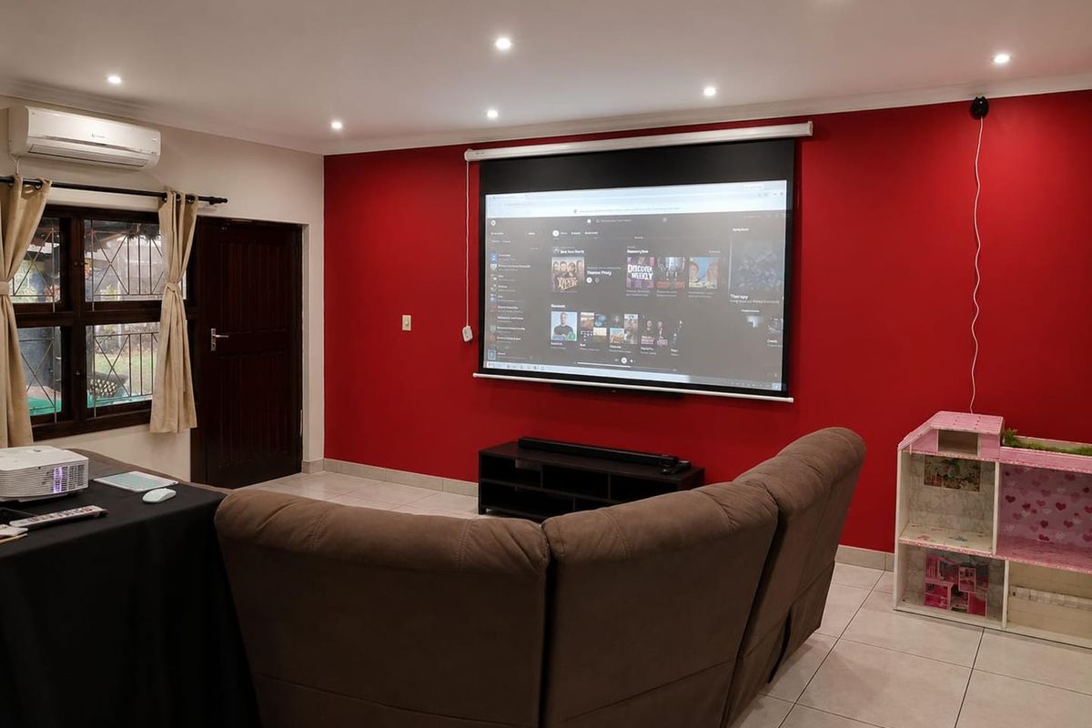 A dedicated cinema room featuring a large projector screen, tiled flooring, recessed lighting, and a wall-mounted split-system air conditioner.