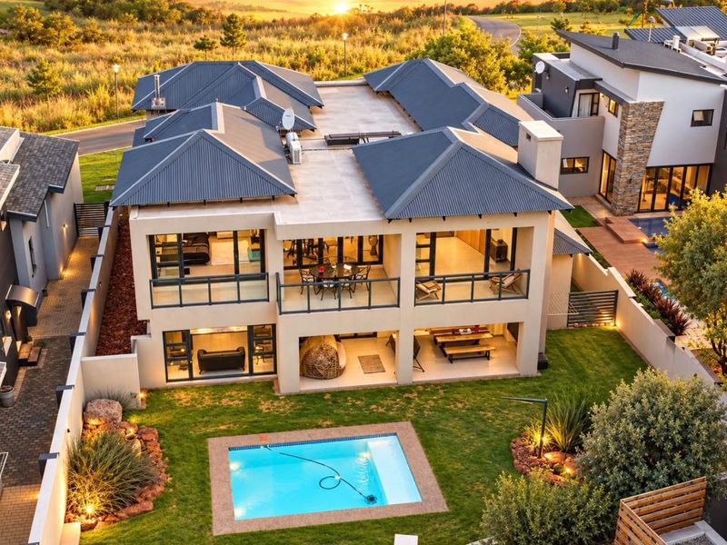 Aerial view of a modern double-story residence featuring a swimming pool, landscaped garden, covered patio, and upper-level balcony with contemporary architectural finishes.