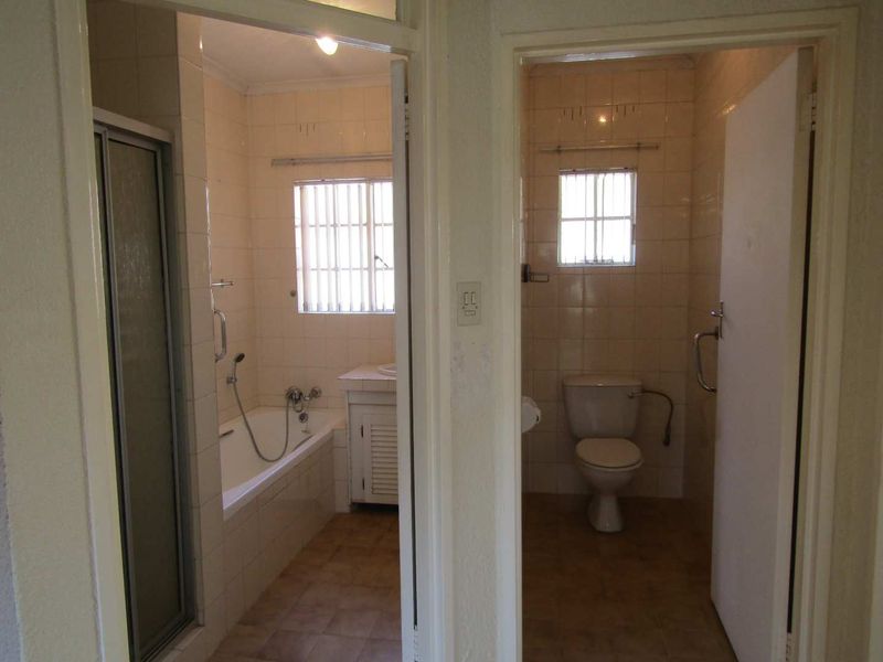 A functional bathroom suite featuring a separate bathtub, shower enclosure, and toilet, with dated tiling and fixtures throughout.