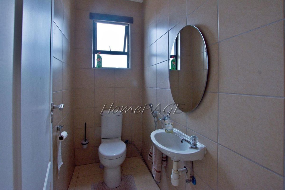 A compact guest bathroom featuring floor-to-ceiling wall tiles, a wall-mounted basin, and a standard toilet.