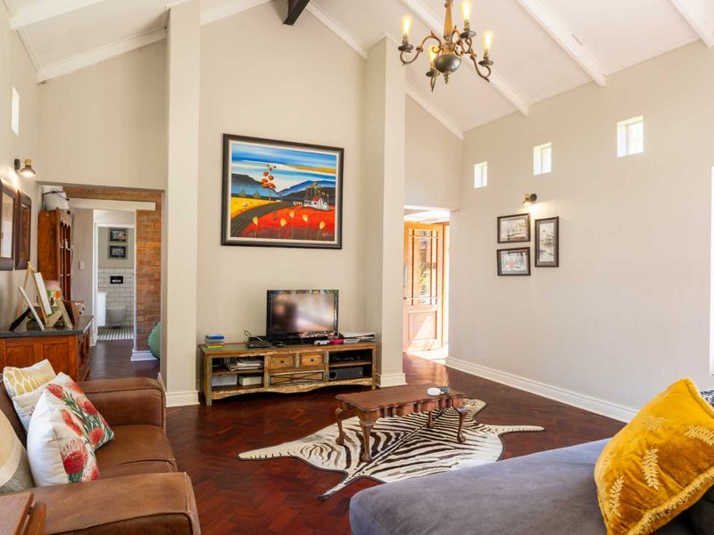 Spacious living room featuring a high vaulted ceiling with exposed beams, elegant herringbone parquet flooring, and warm ambient lighting.