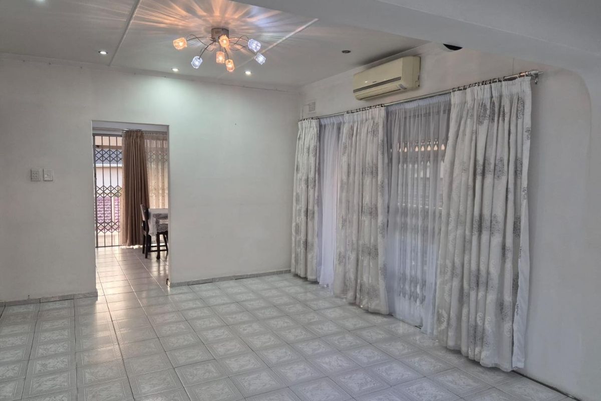 A spacious, light-filled living area featuring neutral tiled flooring, a wall-mounted air conditioning unit, and direct access to an outdoor space via sliding doors.