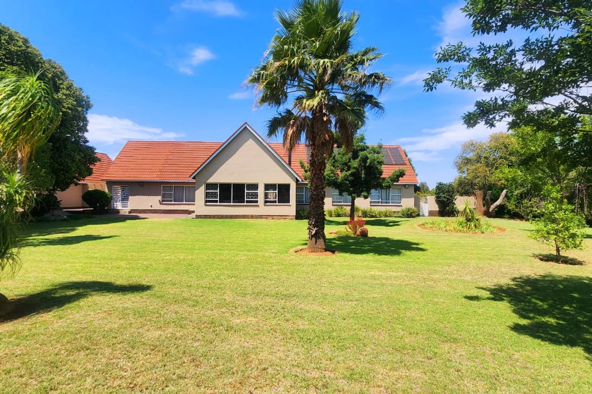 A spacious rear garden view featuring a well-maintained lawn, mature trees, and the rear elevation of the house with a tiled roof and solar panels.
