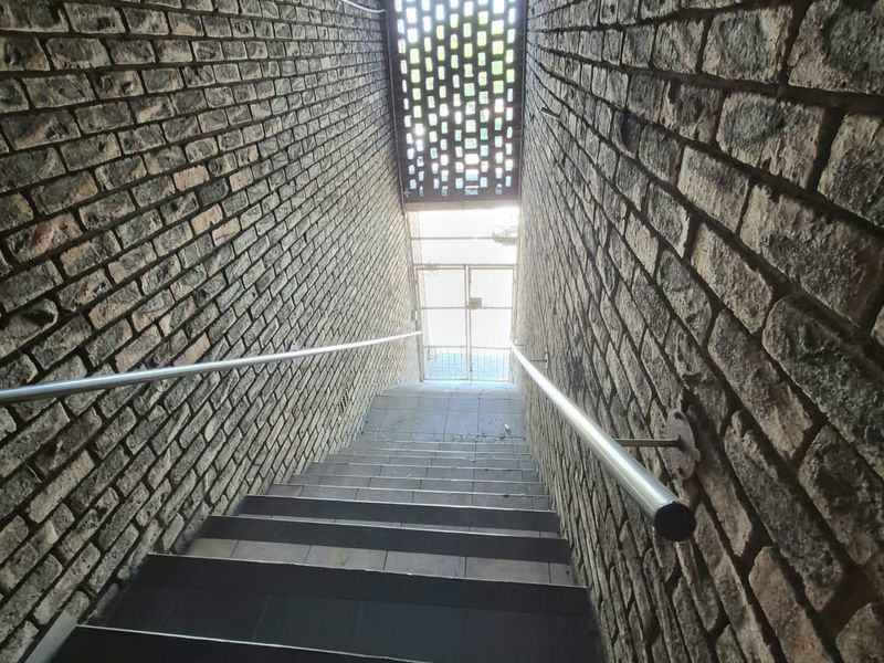 A stairwell featuring exposed brick walls, metal handrails, and a decorative brick screen leading to a secure metal gate entrance.