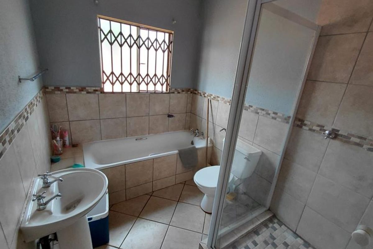 A functional bathroom featuring a pedestal basin, built-in bathtub, separate shower enclosure, and tiled finishes throughout.