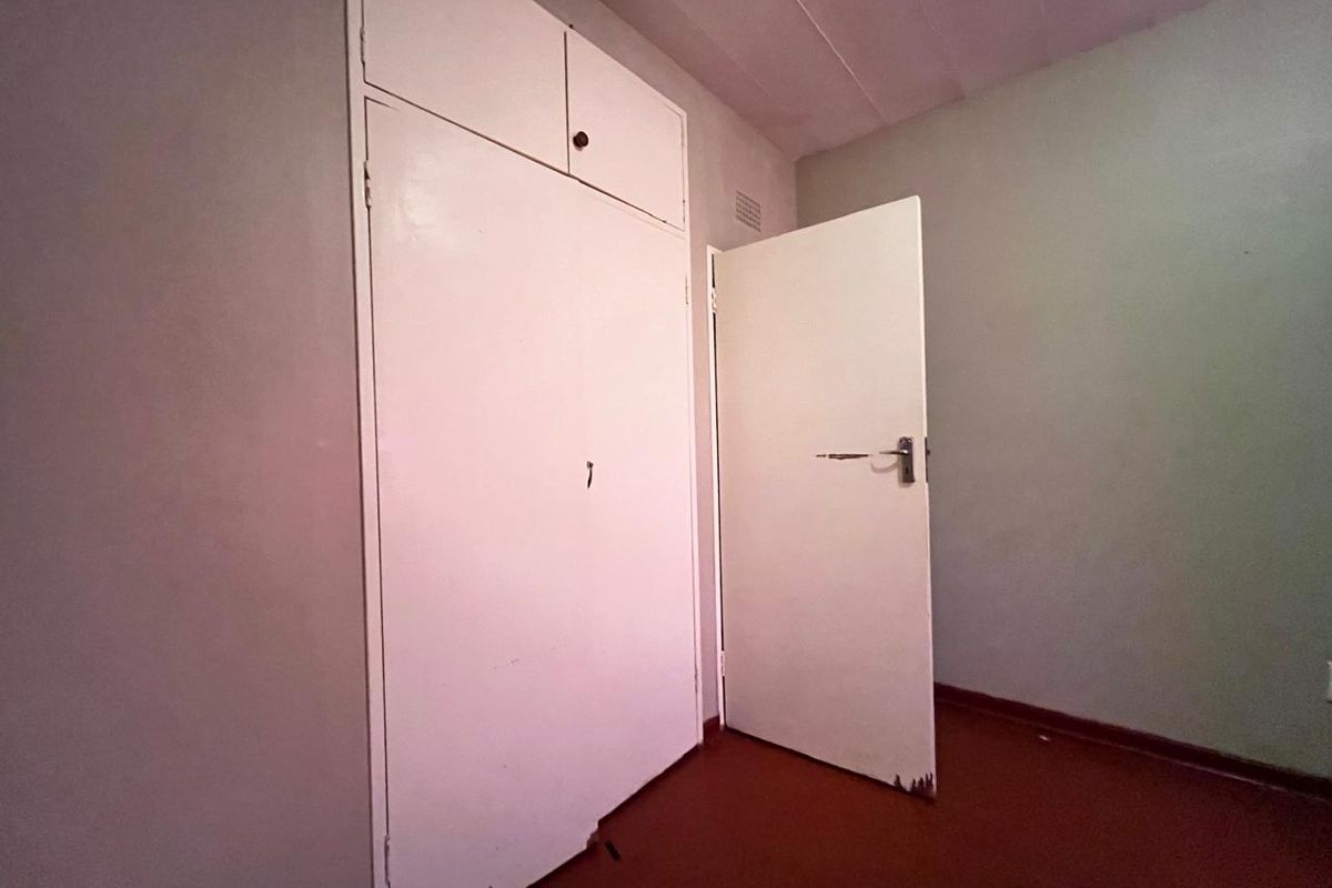 A vacant bedroom featuring built-in storage cupboards and a standard interior door, showcasing original flooring and neutral wall finishes.
