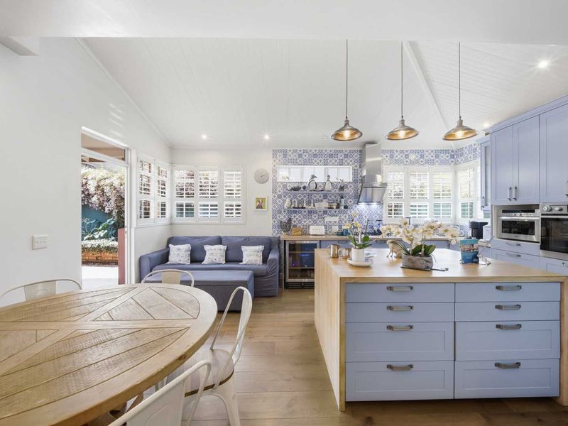 Spacious open-plan kitchen and living area featuring a large central island, modern built-in appliances, timber flooring, and stylish blue cabinetry with decorative tiled splashbacks.