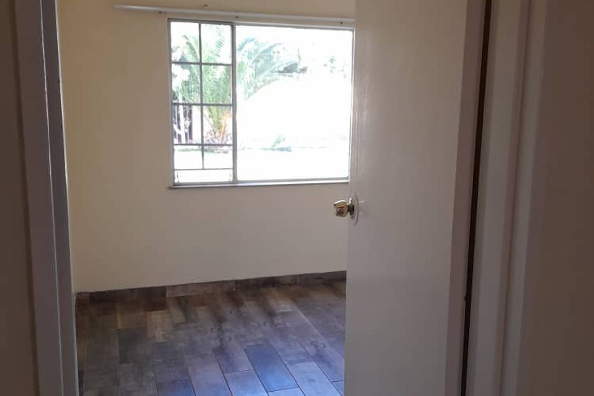 A view into an empty bedroom featuring wood-look tile flooring, a window with security bars, and a ceiling fan.