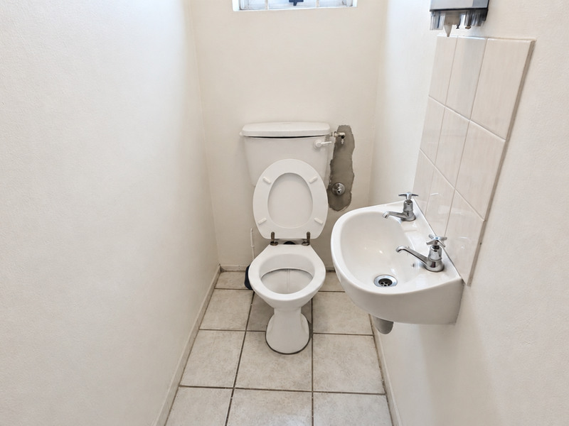 A compact office restroom featuring a standard toilet and wall-mounted basin with tiled splashback.