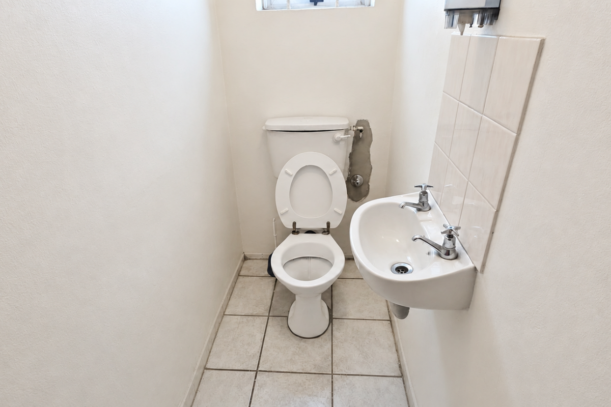 A compact office restroom featuring a standard toilet and wall-mounted basin with tiled splashback.