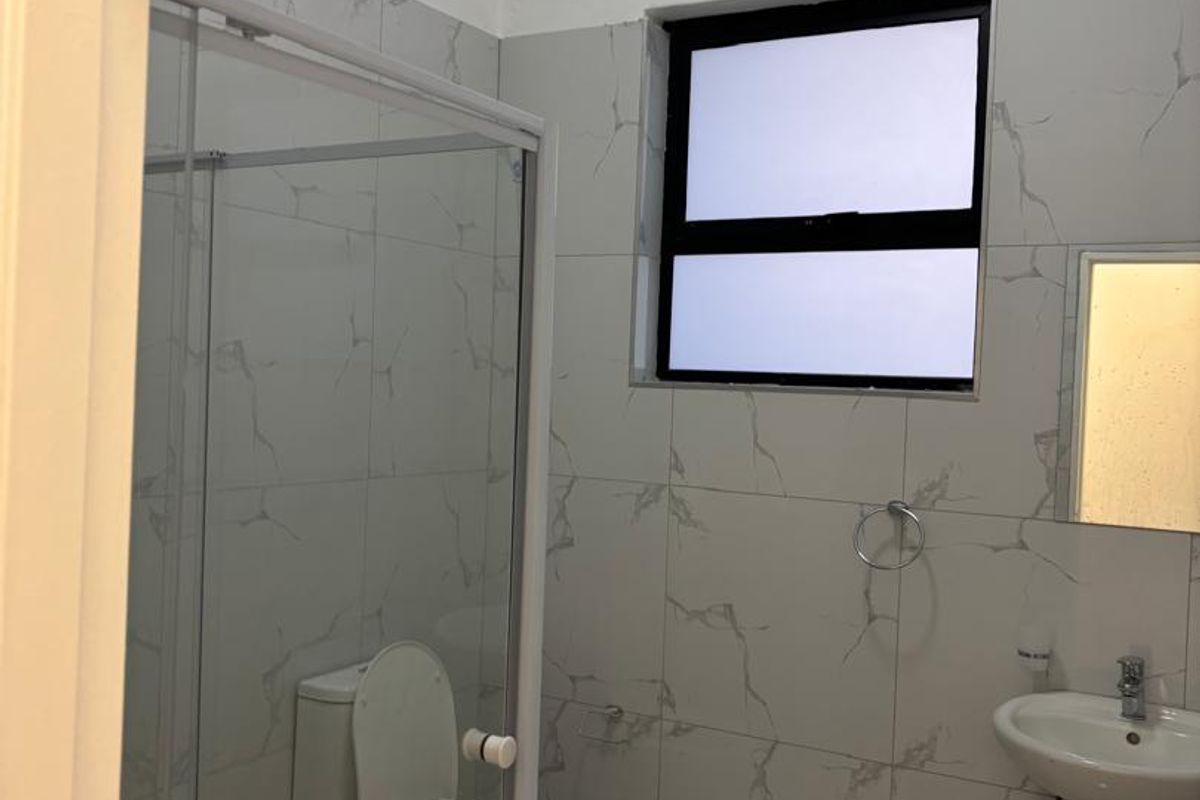 A clean, modern bathroom featuring a pedestal basin, toilet, and a glass-enclosed shower with marble-look wall and floor tiles.