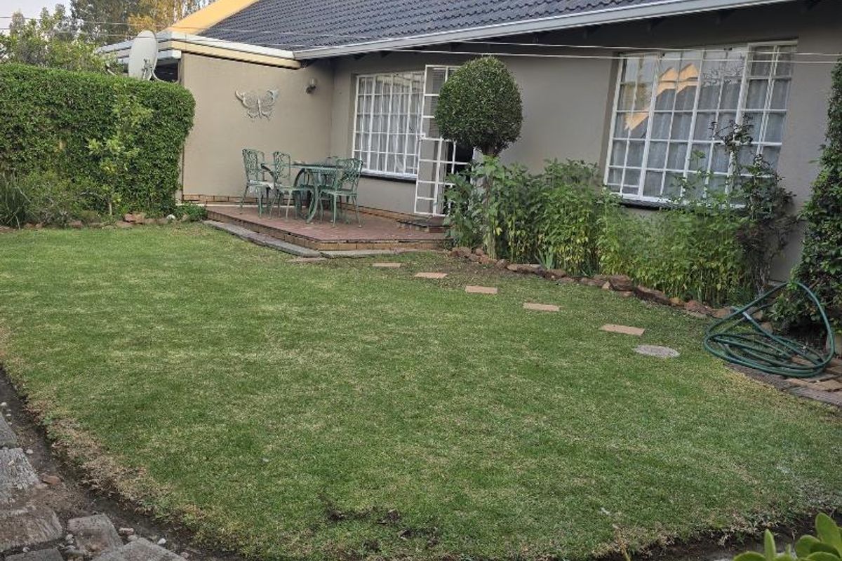 A well-maintained rear garden featuring a manicured lawn, a paved patio area, and a tiled roof townhouse exterior.