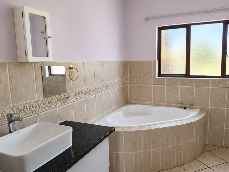 A clean, well-maintained bathroom featuring a corner bathtub, a modern vessel sink on a granite vanity, and neutral wall tiling.