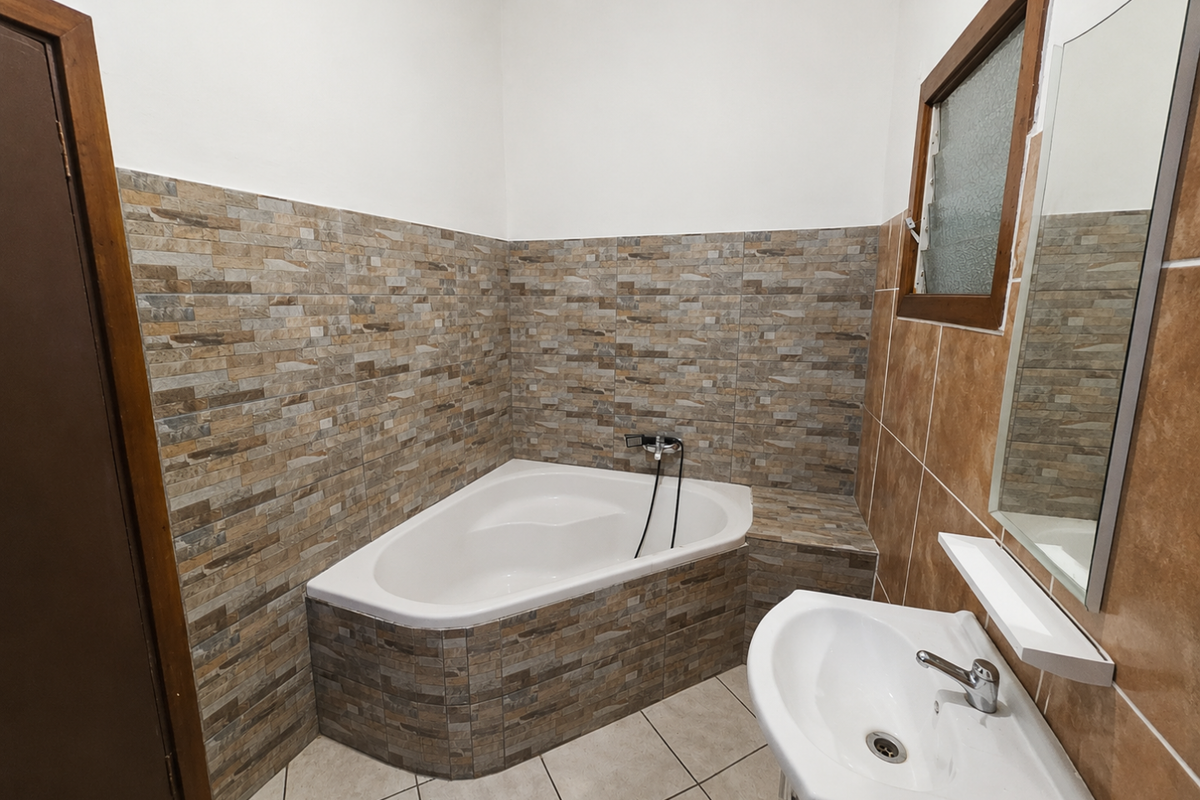 A bathroom featuring a corner bathtub with stone-look tiled surround, a pedestal basin, and a wall-mounted mirror.