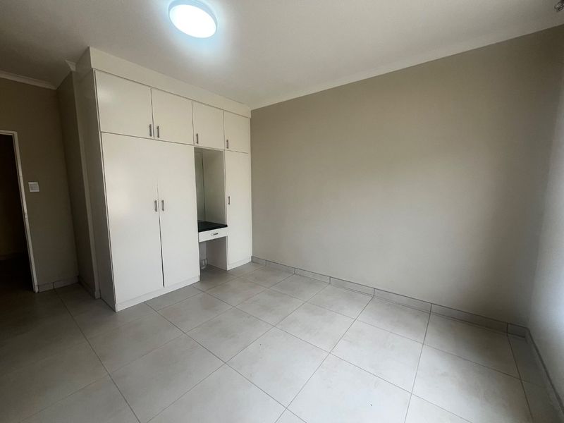 A clean, empty bedroom featuring neutral tiled flooring and white built-in cupboards with an integrated vanity area.