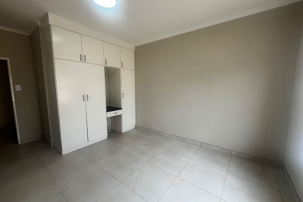 A clean, empty bedroom featuring neutral tiled flooring and white built-in cupboards with an integrated vanity area.