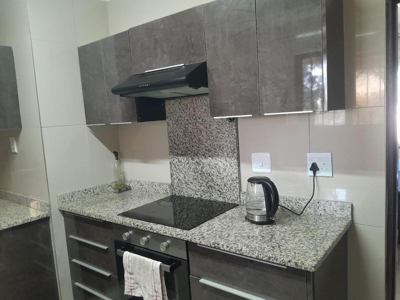 Modern kitchen featuring dark grey cabinetry, granite countertops, a built-in oven, and an electric hob with a matching extractor fan.