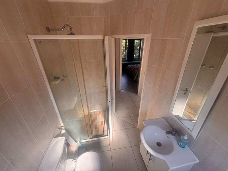 A functional bathroom featuring a shower enclosure, vanity basin, and toilet, finished with neutral wall and floor tiling.