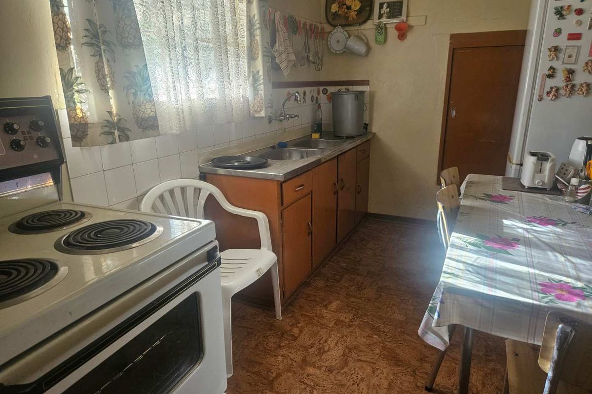 A functional kitchen featuring original wooden cabinetry, a stainless steel sink, and tiled splashbacks, offering potential for modernization and renovation.