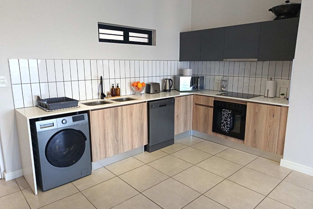 Modern kitchen featuring wood-grain cabinetry, dark grey upper cabinets, integrated oven, hob, extractor fan, and tiled backsplash with a double sink.
