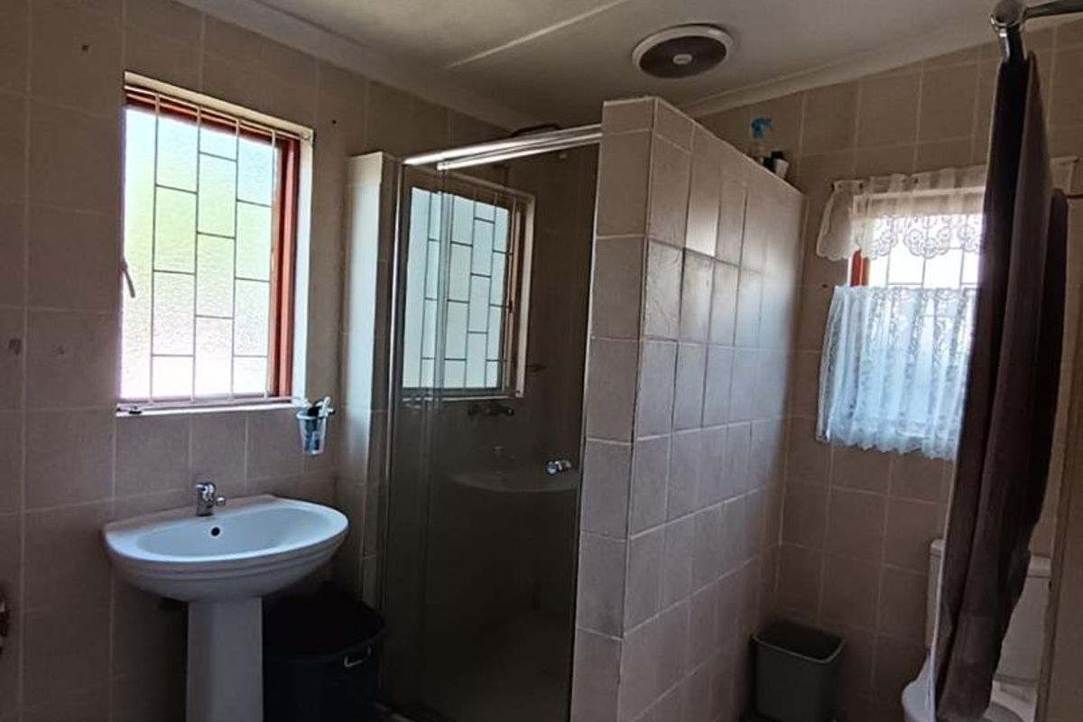 A functional bathroom featuring a pedestal basin, a tiled shower enclosure, and a toilet, finished with neutral wall tiles and tiled flooring.