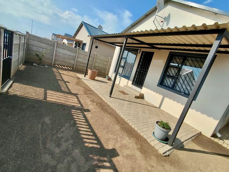 Rear exterior view featuring a covered paved patio, security gates, burglar bars, and a fenced garden area with boundary walls.