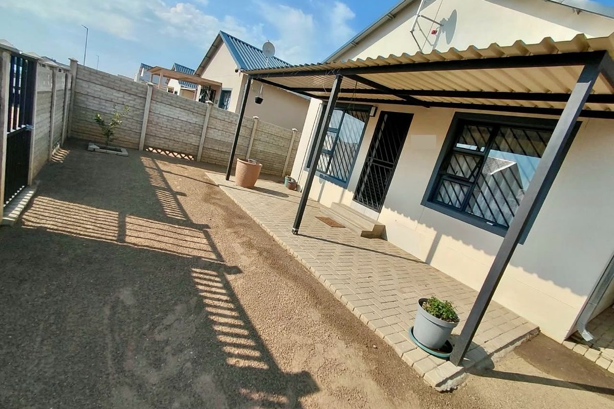 Rear exterior view featuring a covered paved patio, security gates, burglar bars, and a fenced garden area with boundary walls.