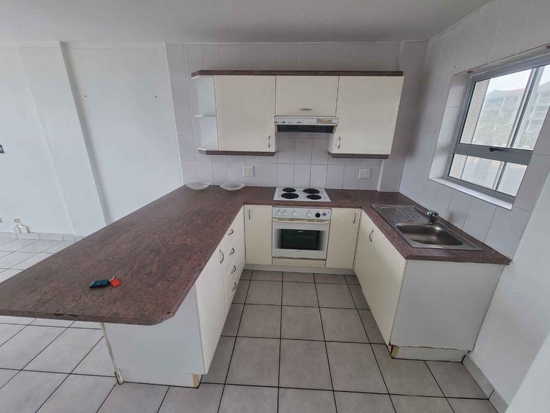 A functional kitchen featuring built-in cabinetry, a laminate countertop, an electric hob with oven, and a stainless steel sink with tiled flooring.