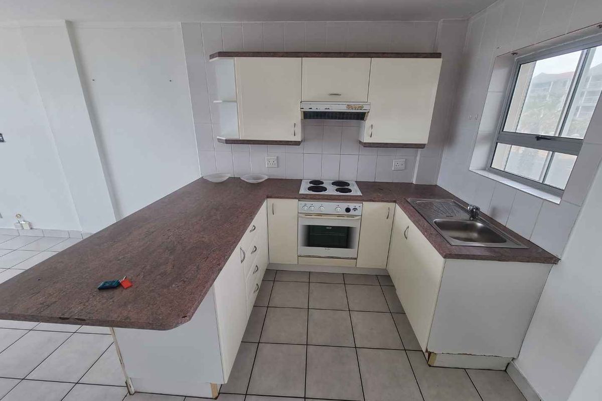 A functional kitchen featuring built-in cabinetry, a laminate countertop, an electric hob with oven, and a stainless steel sink with tiled flooring.
