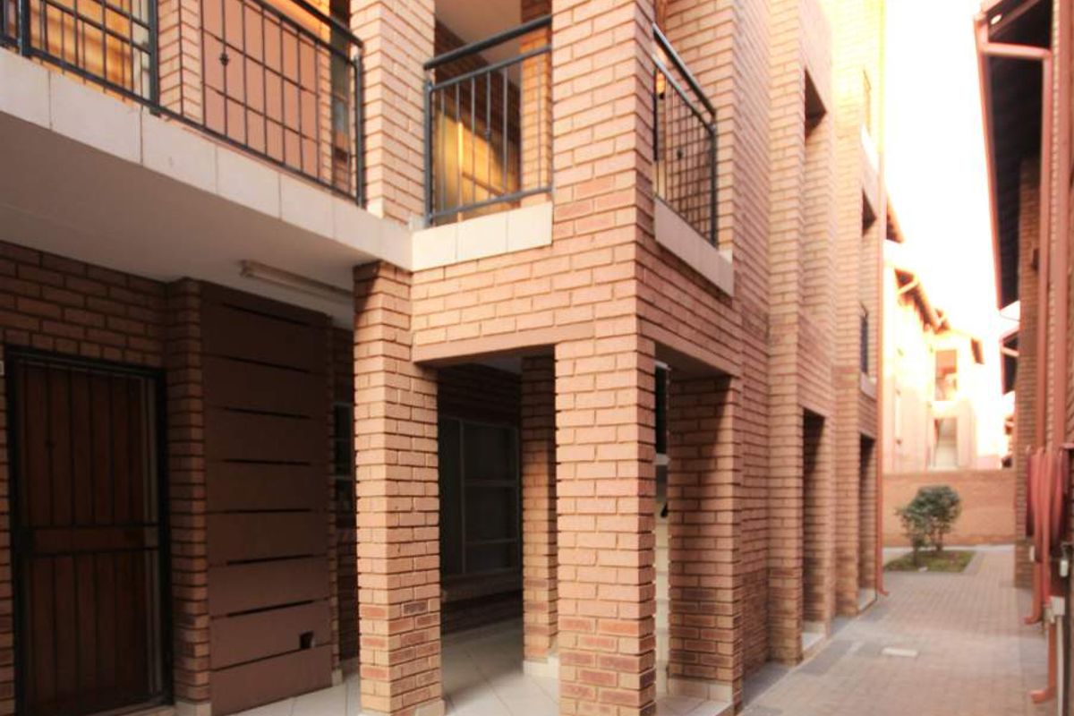 Exterior view of an apartment complex featuring exposed brick architecture, paved walkways, and private balconies with metal railings.
