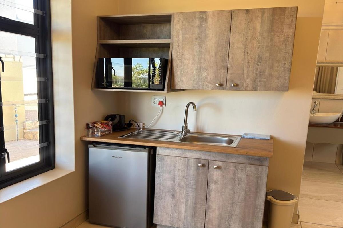 A compact kitchenette area featuring wood-look cabinetry, a stainless steel sink, and tiled flooring, situated adjacent to a window.