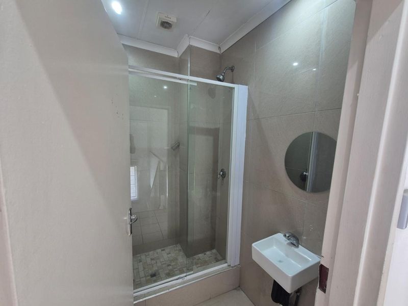 Compact bathroom featuring a glass-enclosed shower, wall-mounted basin, and neutral wall tiling.