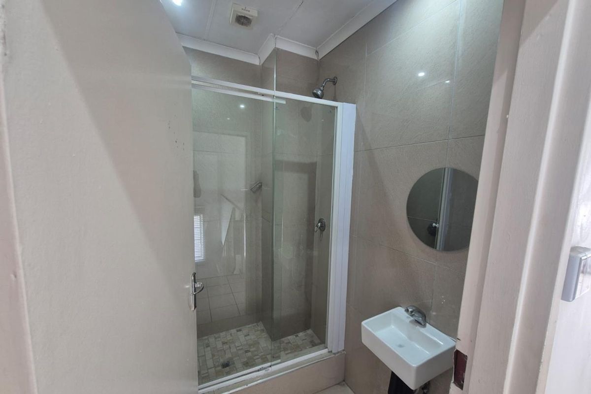 Compact bathroom featuring a glass-enclosed shower, wall-mounted basin, and neutral wall tiling.