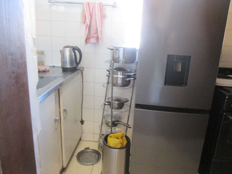 A compact kitchen area featuring a stainless steel sink, tiled backsplash, and built-in cabinetry, currently showing signs of wear and dated finishes.