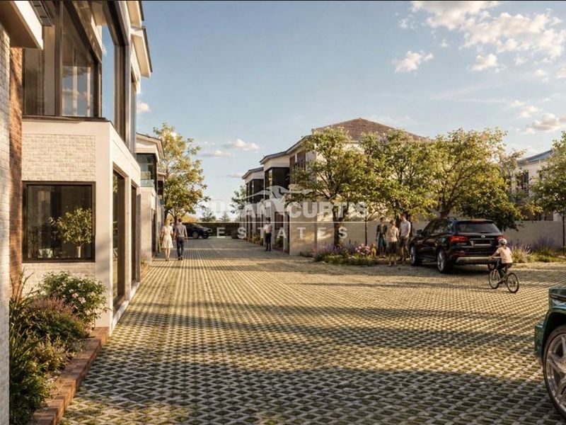 A modern townhouse complex featuring a paved driveway, brick exterior facades, and large windows in a well-landscaped residential setting.