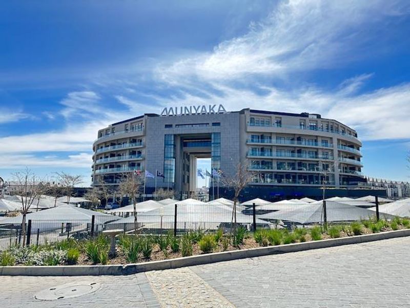 A modern multi-story apartment complex featuring a prominent glass facade, private balconies, and extensive shade-covered parking facilities.