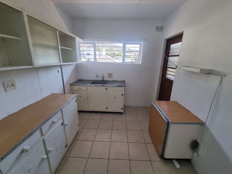 A dated, empty kitchen featuring original built-in cabinetry, a stainless steel sink, and tiled flooring, offering significant potential for a modern renovation.