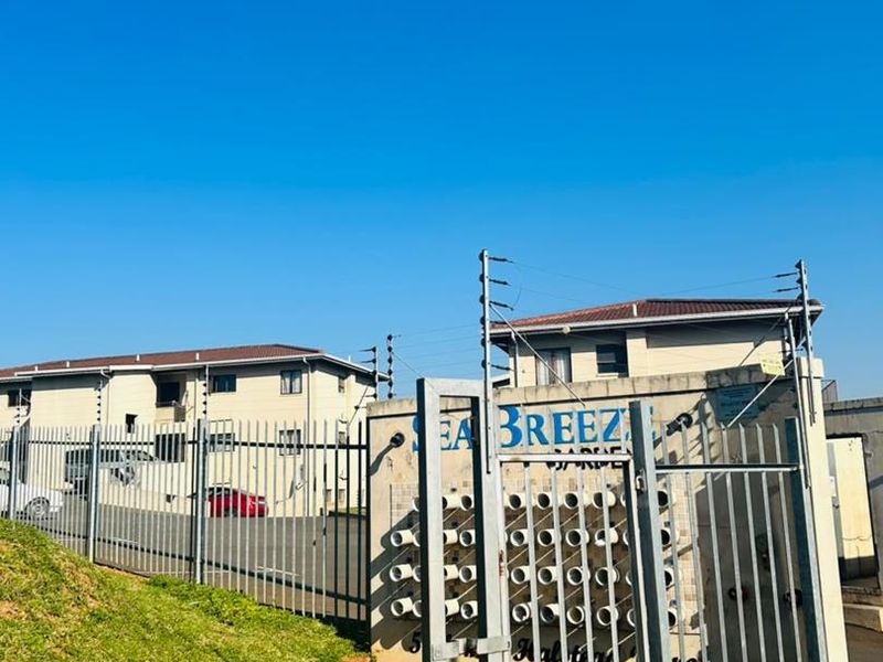Front entrance view of the Sea Breeze apartment complex featuring secure metal gates, perimeter electric fencing, and integrated post boxes.