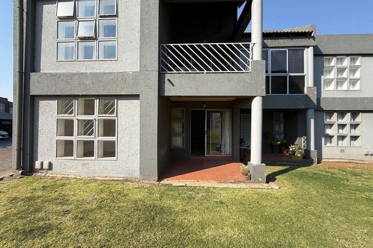 Rear view of a townhouse featuring a ground floor patio, upper balcony, and large aluminium-framed windows overlooking a private garden area.