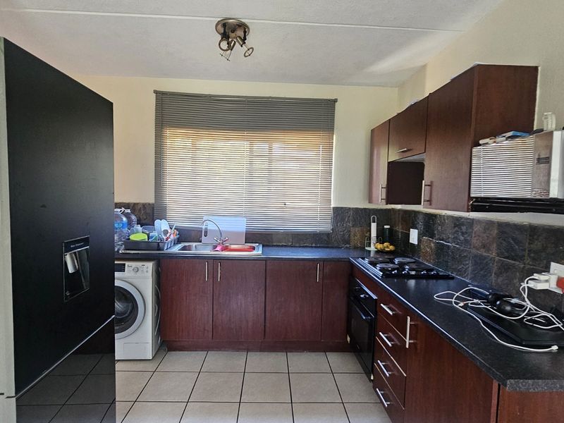 Functional kitchen featuring dark wood cabinetry, laminate countertops, tiled backsplash, and integrated oven and hob, offering a practical layout for daily use.