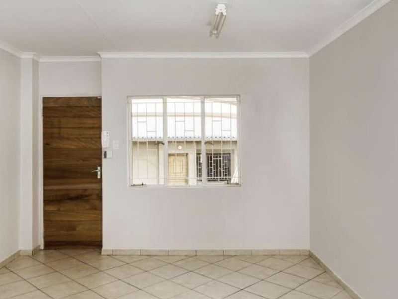 A bright, empty living area featuring neutral walls, tiled flooring, and a secure window with burglar bars.