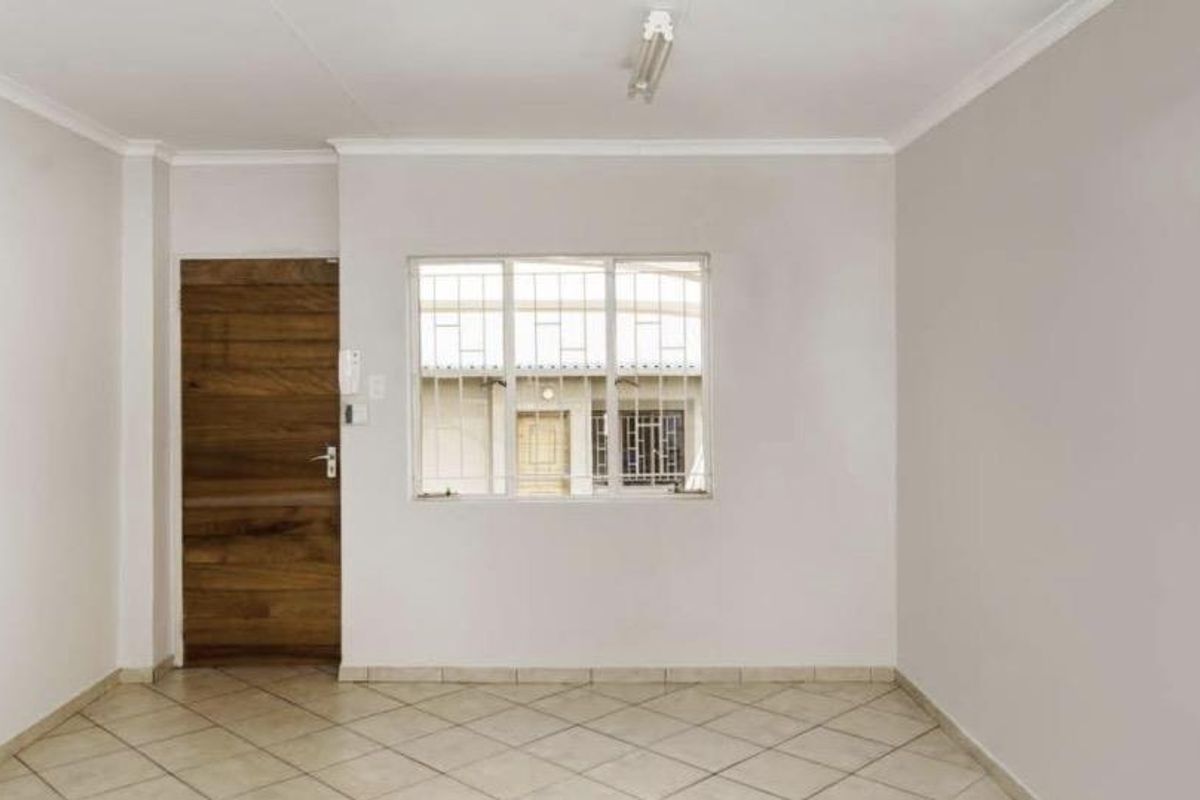 A bright, empty living area featuring neutral walls, tiled flooring, and a secure window with burglar bars.