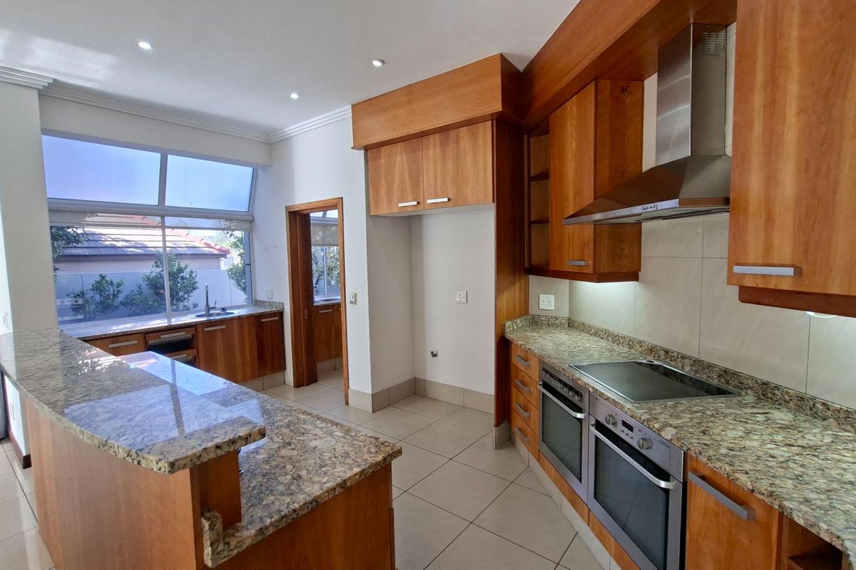 Spacious kitchen featuring granite countertops, wooden cabinetry, built-in double oven, electric hob, and stainless steel extractor fan with tiled flooring throughout.