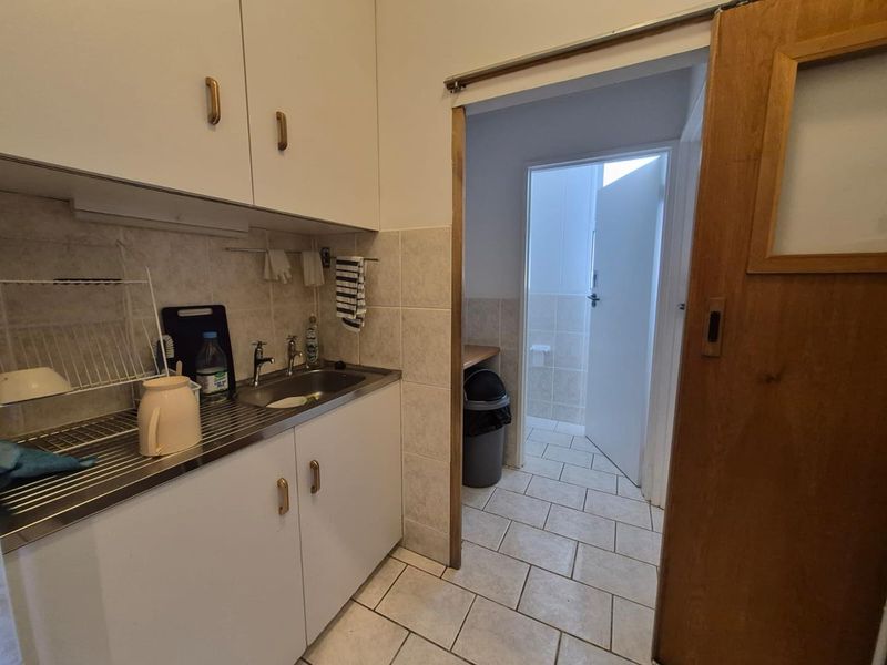 A functional scullery area featuring built-in cabinetry, a stainless steel sink, tiled splashbacks, and a sliding wooden door leading to an adjacent utility space.