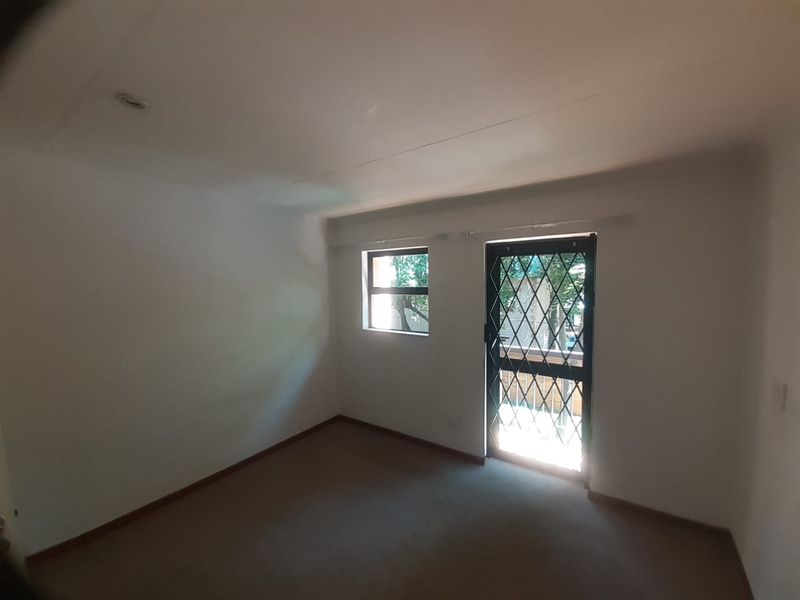 A vacant bedroom featuring neutral carpeting, a security gate on the door, and a window providing natural light.