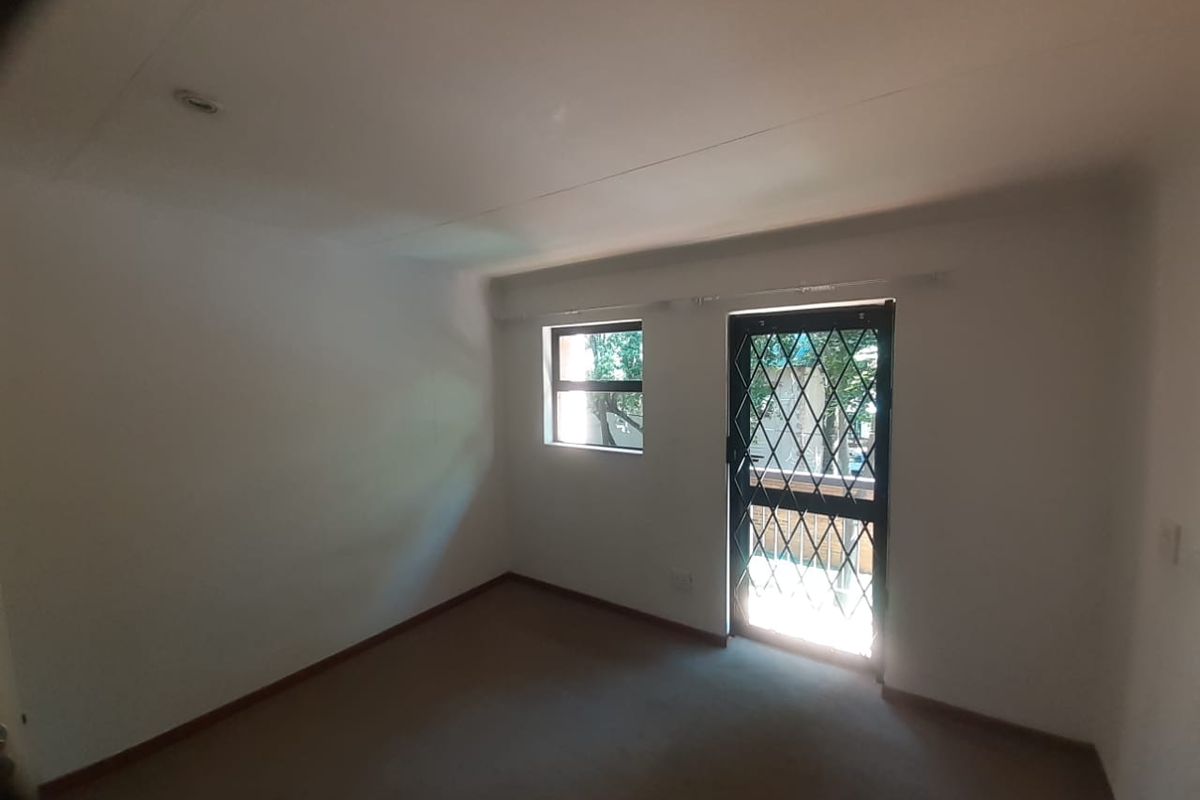 A vacant bedroom featuring neutral carpeting, a security gate on the door, and a window providing natural light.