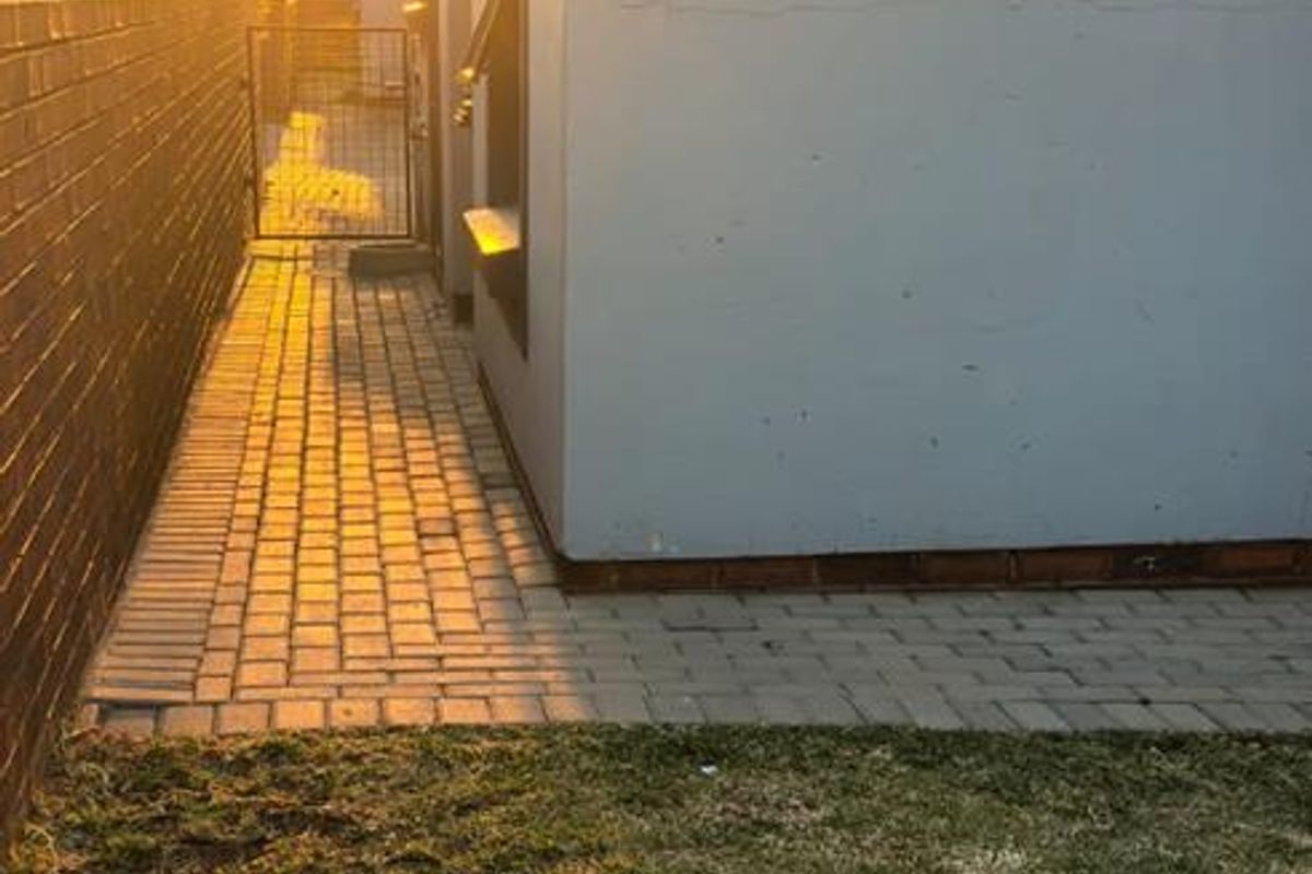A side view of the property featuring a paved walkway, brick boundary wall, and a small lawn area at sunset.